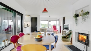 A modern living room with a round dining table, colorful chairs, a fireplace, and a large window. - "Clarita" - 300m to the fjord by Interhome (Roslev)