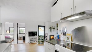 A modern kitchen with white cabinets, a built-in stove, and a dining area with a chair and table. - "Clarita" - 300m to the fjord by Interhome (Roslev)