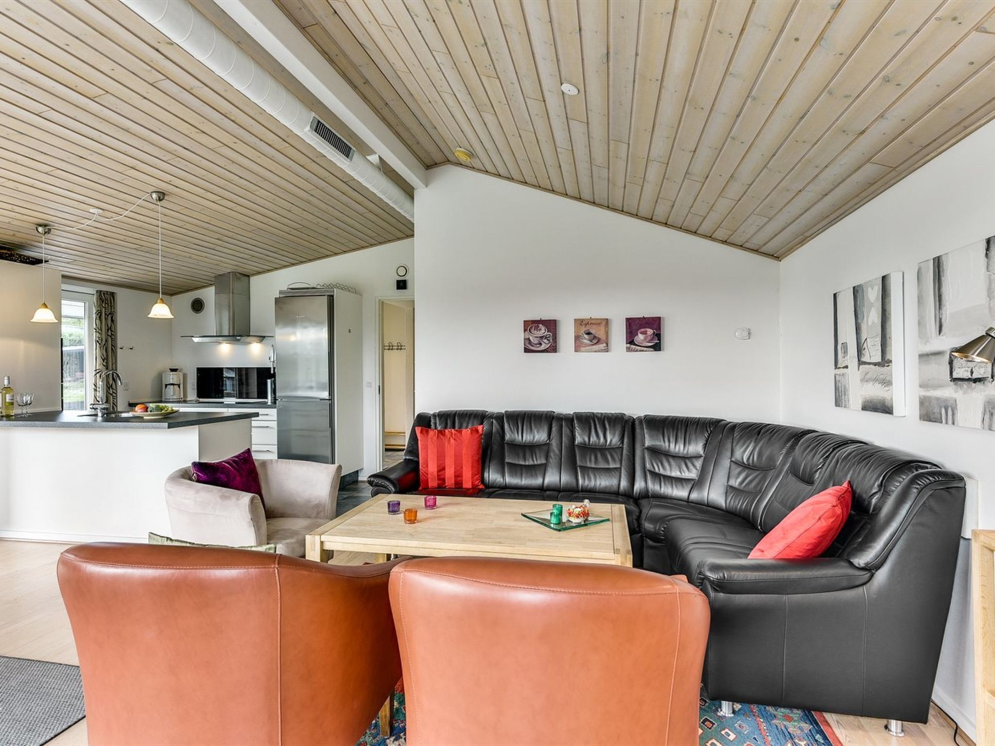 Un salon moderne avec un canapé en cuir noir, un plafond en bois et une cuisine en arrière-plan.