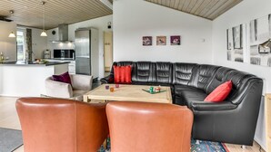 Un salon moderne avec un canapé en cuir noir, un plafond en bois et une cuisine en arrière-plan.