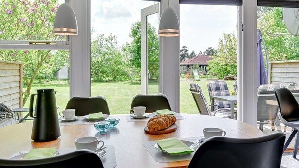 Ein Essbereich mit Tisch für vier Personen, großen Fenstern und Blick auf Garten und Haus.