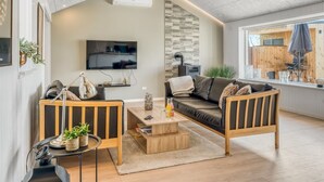 Een moderne woonkamer met een bank, twee fauteuils, een salontafel en een aan de muur bevestigde televisie.