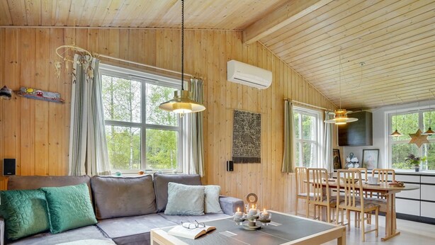 A cozy cabin interior with a wooden ceiling, a sofa with cushions, a dining table, and a kitchen area.