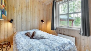 A wooden-paneled room with a bed, a window, and a bookshelf.