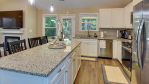A modern kitchen with granite countertops, white cabinets, a stainless steel refrigerator, and a built-in oven. - Charming Pendleton Retreat ~ 5 Mi to Clemson! (Pendleton)