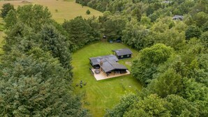 Une grande maison entourée d’une forêt dense, avec une pelouse bien entretenue et un espace patio.