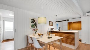 Une cuisine moderne avec des meubles blancs, un îlot central en bois et un coin repas comprenant une table et des chaises blanches.