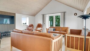 Een ruime woonkamer met een hoge plafond, leren banken, een houten vloer en een groot raam met uitzicht op groen.
