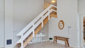 Een trap met houten leuningen en een stenen muur, die leidt naar een kamer met een witte tafel en een bank.
