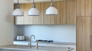 Una cocina con armarios de madera, encimera blanca, pileta integrada y tres lámparas colgantes.