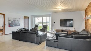A modern living room with a large black leather sofa, a flat-screen TV mounted on the wall, and a large window offering a view of the outdoors. - "Rahild" - 2km to the fjord by Interhome (Thyholm)