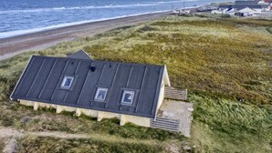 Uma casa costeira com telhado inclinado, uma pequena varanda e vista para a praia e o oceano.