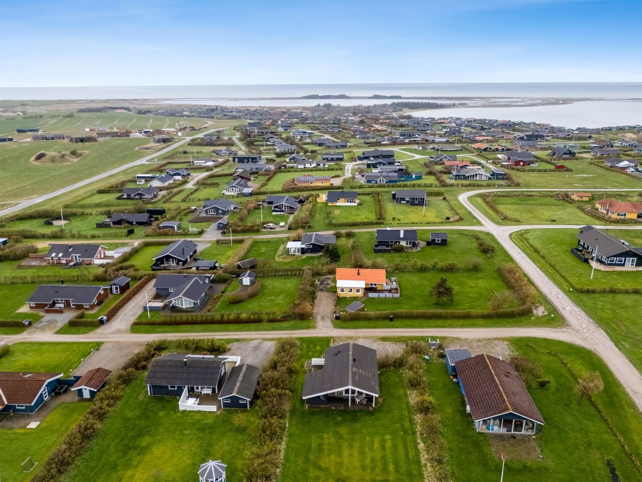 Vista aérea de una zona residencial con casas, caminos y una masa de agua al fondo.