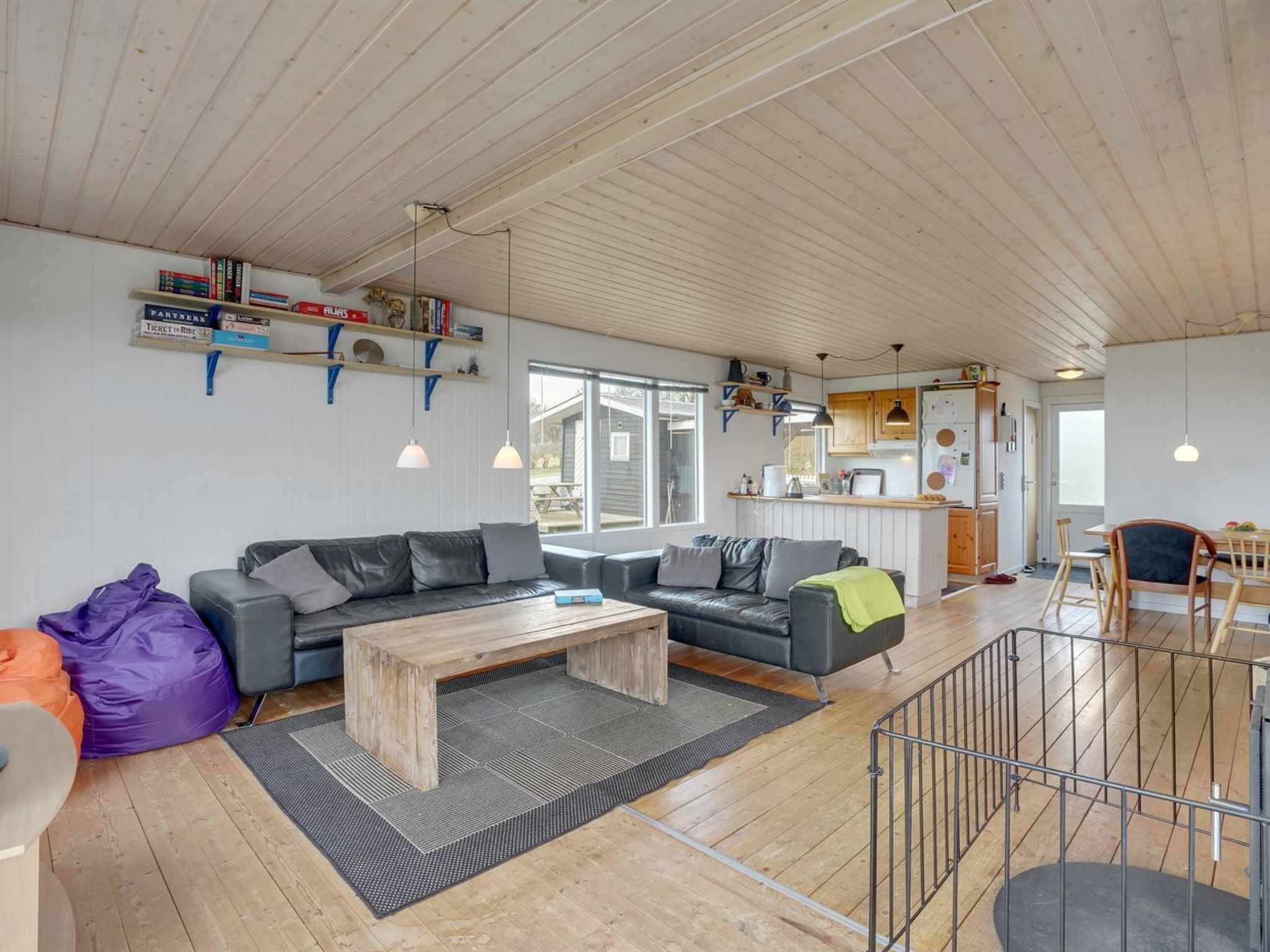 A spacious living area with a wooden ceiling, a sofa, a coffee table, and a dining area with a wooden table and chairs.
