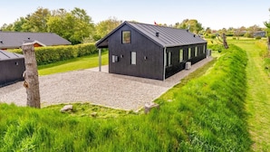 Een modern gebouw met een donkere gevel, een grindpad en een verzorgd gazon.