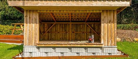 A wooden structure with a sloped roof, a stone base, and a bench area.