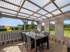 An outdoor patio with a covered dining area, a wooden fence, and a view of the surrounding landscape.