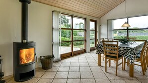 A room with a wood-burning stove, a dining table with chairs, and large windows offering a view of the outdoors. - "Kyllikki" - 300m to the fjord by Interhome (Børkop)