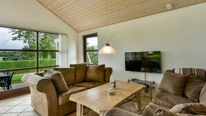 A spacious living room with a large window, a wooden ceiling, and a flat-screen TV mounted on the wall. - "Kyllikki" - 300m to the fjord by Interhome (Børkop)