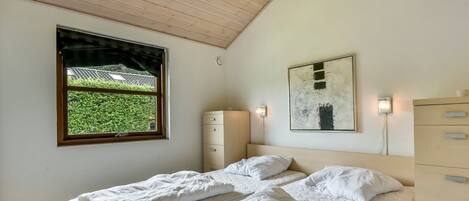 Een slaapkamer met een bed, een kaptafel, een nachtkastje, een raam met uitzicht en een schilderij aan de muur.