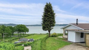 Ein Haus mit Seeblick, ein hoher Baum und ein gepflasterter Weg zum Haus.