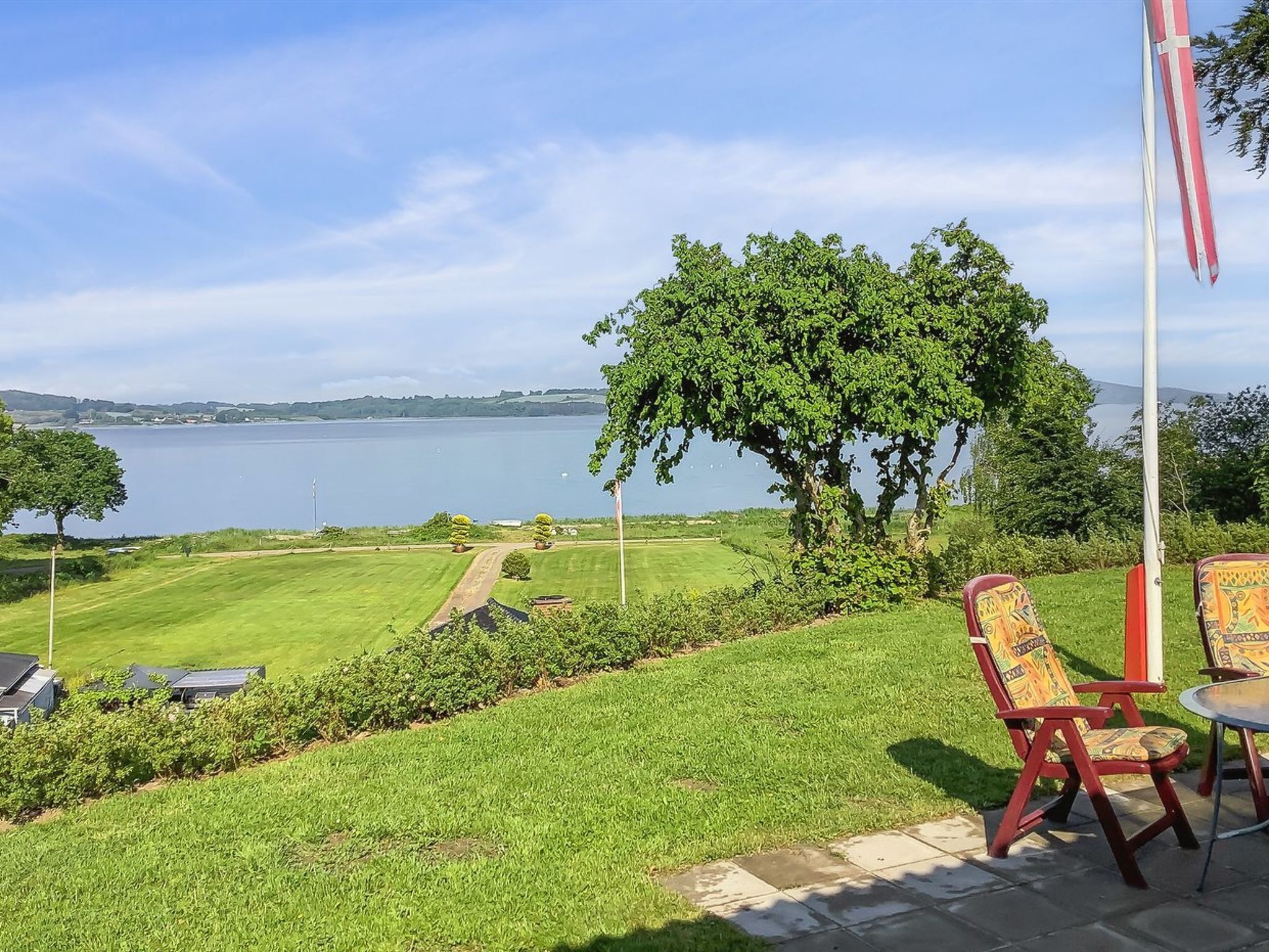 Un patio con mesa y sillas, un asta de banderas y vista a un lago.