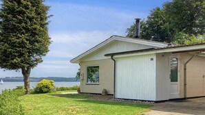 Ein eingeschossiges Haus mit weißer Fassade, einer Garage und Blick auf einen See.