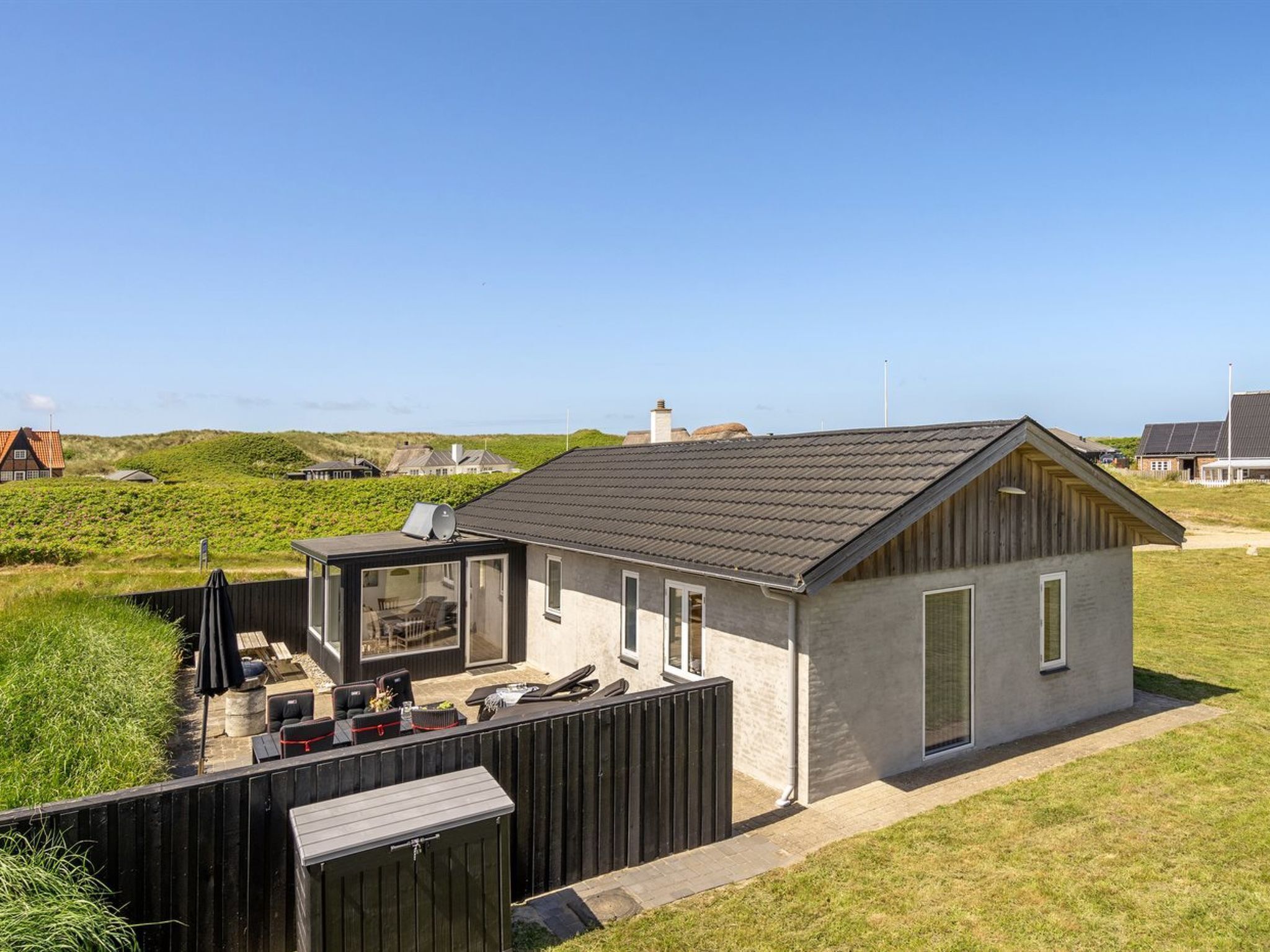 Une maison moderne dotée d’une grande terrasse vitrée, d’une plateforme en bois et offrant une vue sur le paysage environnant.