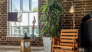 Ein Zimmer mit Backsteinwand, einem Holzschaukelstuhl, einem Blumentopf, einer Lampe und einem Fenster mit Jalousien.