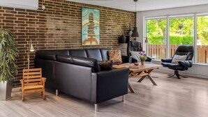 Ein modernes Wohnzimmer mit Backsteinwand, einer schwarzen Ledersofa, einer Holzbank, einem schwarzen Sessel und einem Couchtisch aus Holz.