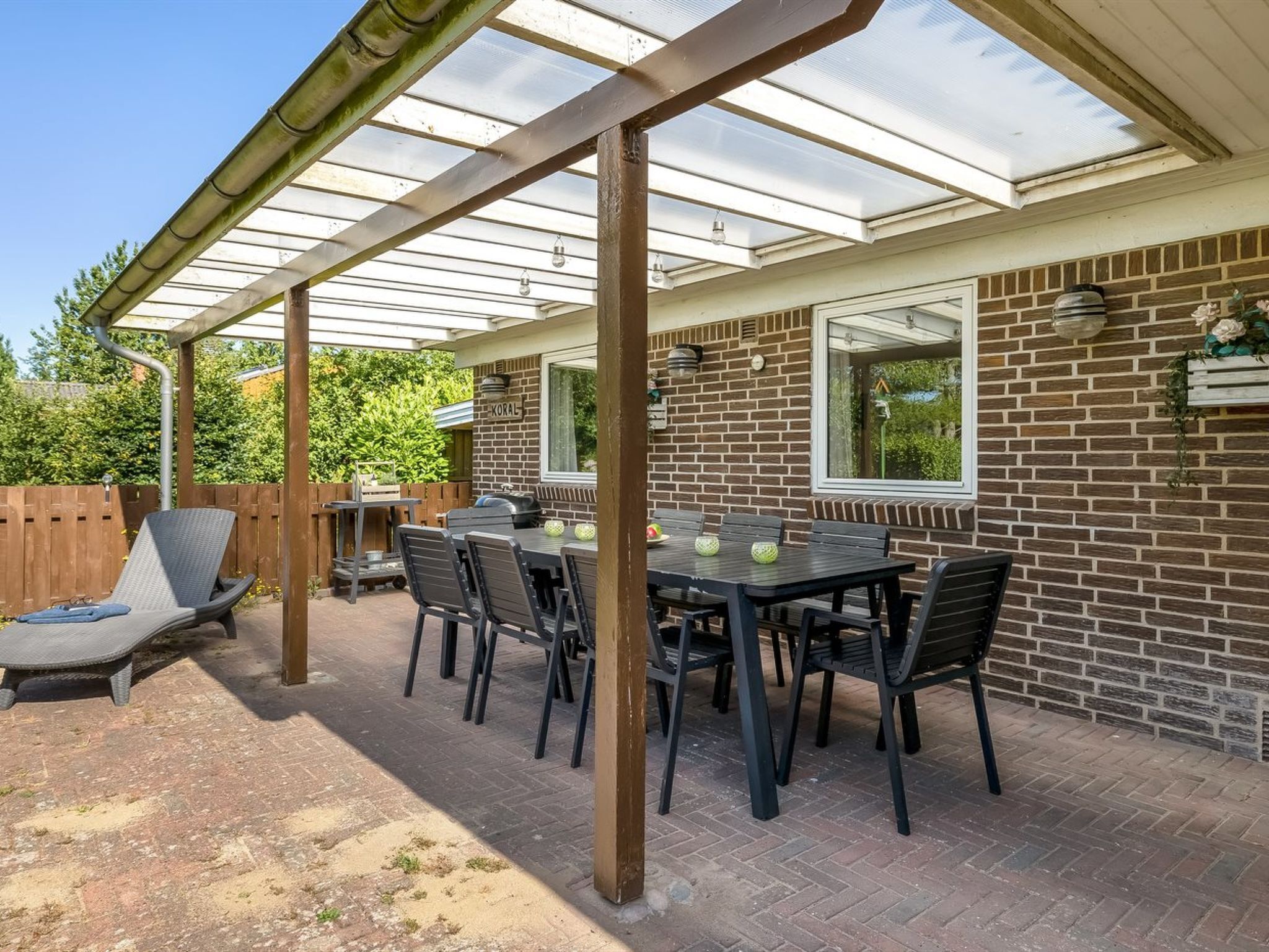 Een overdekt terras met een bakstenen muur, een tafel met stoelen en een barbecue.