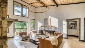 A modern interior with a stone wall, a large window, a wooden ceiling, and a central seating area with a sofa and a coffee table. - Morgan Trail - Hot tub & ping pong table (Blue Ridge Mountains)