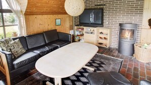 A cozy cabin interior with a black leather sofa, a round table, a TV, a wooden chest of drawers, and a wood-burning stove. - "Ilva" - 300m to the fjord by Interhome (Ulfborg)