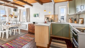 Una cocina moderna con vigas de madera, un comedor con mesa y sillas, y una alfombra colorida.