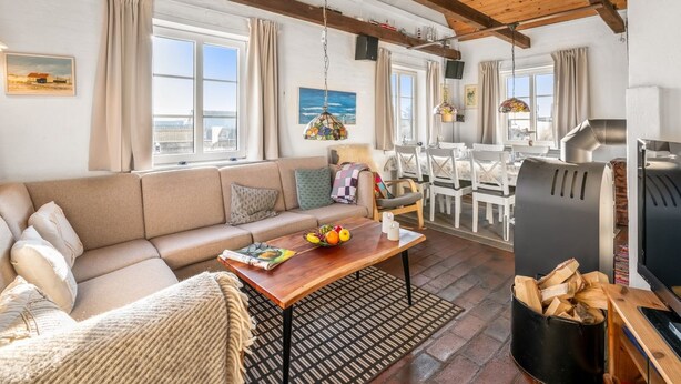 Una sala de estar acogedora con un sofá, una mesa de centro y un comedor. Hay una chimenea, un televisor y una ventana con cortinas.