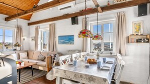 Comedor con una mesa dispuesta para cuatro, sillas blancas, techo de madera y vistas al exterior a través de amplios ventanales.
