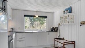 Eine moderne Küche mit weißen Schränken, einem Fenster mit Blick auf Bäume, einer Kaffeemaschine und einem Holzwagen mit Korb.
