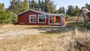 Eine rote Holzhütte mit Veranda und Hinweisschild Nummer 25, umgeben von Bäumen und einer Rasenfläche.