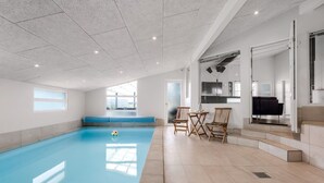 Ein geräumiger, überdachter Pool mit blauem Boden, Holzstühlen und einer Sitzbank.
