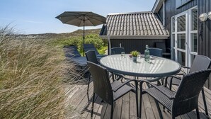 Eine Terrasse mit einem runden Glastisch, Korbstühlen und einem großen Sonnenschirm.