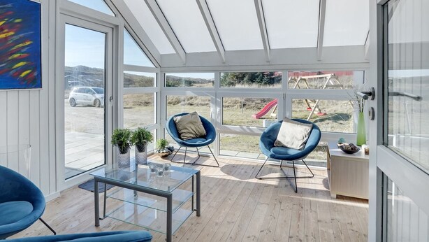 Ein modernes Zimmer mit einem Glastisch, zwei blauen Stühlen und Blick auf einen Spielplatz.