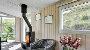 A modern room with a black leather sofa, a round table with candles, a large window with a view of greenery, and a wood-paneled wall with framed pictures. - "Jess" -  from the sea by Interhome (Ringkøbing)