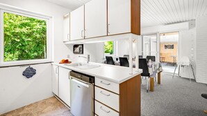 Une cuisine moderne avec des meubles blancs, un lave-vaisselle et une grande fenêtre donnant sur un paysage verdoyant.