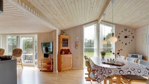 Een ruime eetruimte met een grote houten tafel, stoelen en een televisie op een standaard.