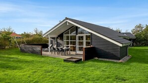 Ein modernes Haus mit Satteldach, einer überdachten Terrasse mit Gartenmöbeln und einem gepflegten Rasen.