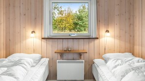 Ein Zimmer mit Holzwänden, zwei Betten, einem Fenster mit Blick auf Bäume und einem Regal mit Gläsern.