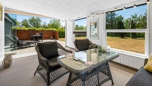 A sunlit room with a glass table and wicker chairs, large windows, and a view of the outdoors. - "Eira" - 350m to the fjord by Interhome (Tarm)