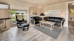 Un salon moderne avec un canapé en cuir noir, un fauteuil assorti et une table basse. Les murs de la pièce sont en bois et le plafond est en pente.
