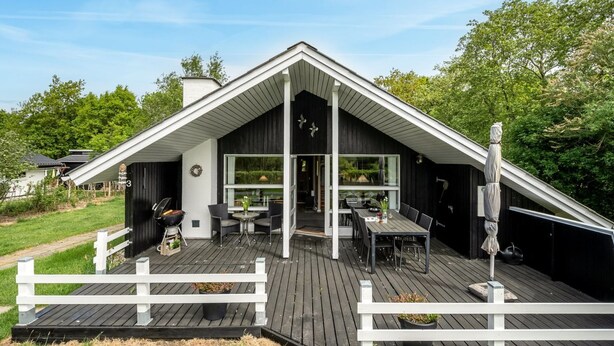 Une maison moderne avec un toit en pente, une terrasse dotée de mobilier d’extérieur et une clôture blanche qui entoure la terrasse.