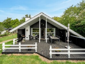 Une maison moderne avec un toit en pente, une terrasse dotée de mobilier d’extérieur et une clôture blanche qui entoure la terrasse.
